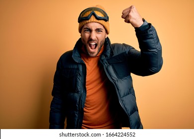 Young Handsome Skier Man With Beard Wearing Snow Sportswear And Ski Goggles Angry And Mad Raising Fist Frustrated And Furious While Shouting With Anger. Rage And Aggressive Concept.