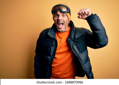 Young Handsome Skier Man Skiing Wearing Snow Sportswear Using Ski Goggles Angry And Mad Raising Fist Frustrated And Furious While Shouting With Anger. Rage And Aggressive Concept.