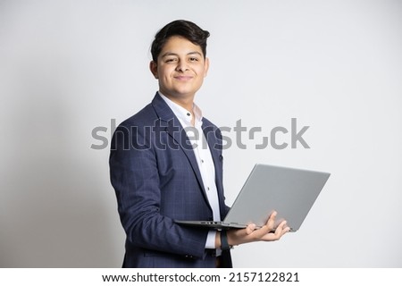 Young handsome smiling Indian teenager boy wearing suit holding laptop at isolated on white studio background. Asian corporate male using computer. cloud computing 