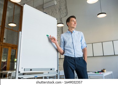 Young Handsome Smiling Man Standing At Empty White Board With Marker, Leadership Business Training In Open Space Office, Successful Modern Youth, Online Education