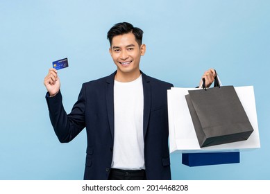 Young Handsome Southeast Asian Millenial Man Holding Credit Card And Bags In Light Blue Studio Isolated Background For Cashless Shopping Concept