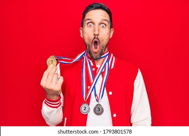 Young Handsome Sportsman Winning Medals Standing Over Isolated Red Background Scared And Amazed With Open Mouth For Surprise, Disbelief Face