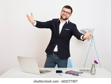 young handsome stylish hipster man in suit at office table, business style, ceo, isolated, laptop, start up, work place, smiling, happy, positive, open arms, greeting