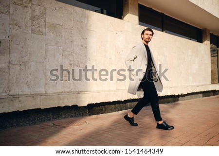 Young handsome stylish man in coat thoughtfully looking away on street
