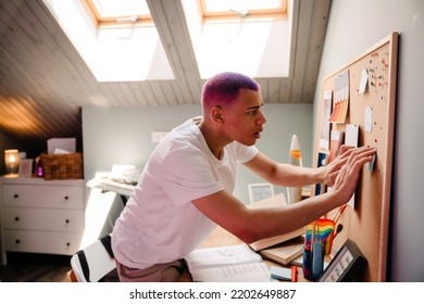 Young Handsome Stylish Serious Boy Pinning Note On Cork Board While Standing In Cozy Room At Home