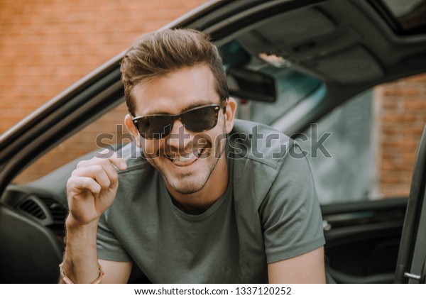 Young handsome and stylish\
white man in luxury car wearing sunglasses. This elegant caucasian\
male model is smiling and looks happy, masculine and confident.\
