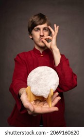 Young Handsome Tall Slim White Man With Brown Hair Doing Chefs Kiss Sign Holding Pu Erh Tea Cake In Red Shirt On Grey Background