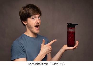 Young Handsome Tall Slim White Man With Brown Hair Looking Excited Pointing At Smoothie Bottle In Grey Shirt On Grey Background