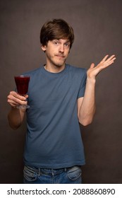 Young Handsome Tall Slim White Man With Brown Hair Holding Wine Cup Not Caring In Grey Shirt On Grey Background