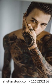 a young handsome tattooed man in the morning shaves in front of a mirror, a razor in his hands, a shave.