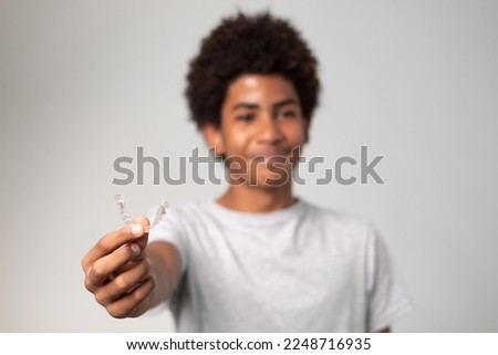 Young handsome teen latin  holding invisible aligner orthodontic  smiling with a happy and cool smile on face. The dental aligner is on focus and his face out of focus