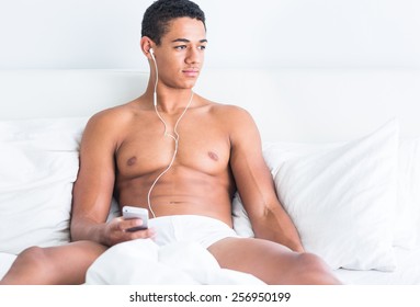 Young Handsome Topless Black Man Enjoying Music In Bed.