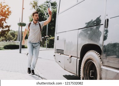 Young Handsome Tourist almost Late for Bus. Man with Backpack Running after Tour Bus and asking Bus Driver to Stop by Waving Hand. Traveling, Tourism and People Concept. Active Lifestyle
