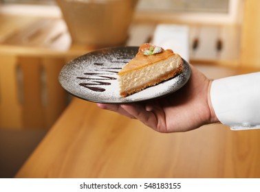 Young handsome waiter holding plate with delicious cake in a restaurant - Powered by Shutterstock