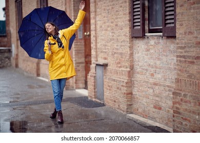 A young handsome woman in a yellow raincoat and with umbrella is dancing while walking the city in a relaxed manner on a rainy day. Walk, rain, city