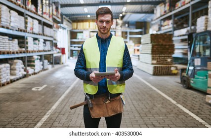 Young handyman or builder standing in the drive through in a hardware warehouse with a tablet in his hand looking at the camera
