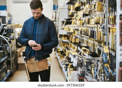 Young Handyman Checking Information On His Mobile Before Making A Purchase In A Hardware Store