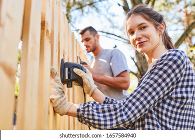 Young Handyman Couple At The Fence Grind In The Garden Of The New House As A Home