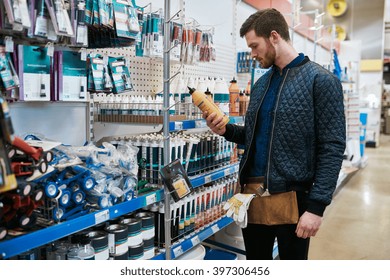 Young handyman or DIY homeowner in a store standing selecting a product in the hardware department and reading the label