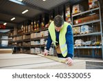 Young handyman working in a building supplies or hardware warehouse checking lumber on a table