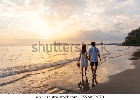 Young happiness Asian couple traveler relaxing and watching beautiful Sunset on the tranquil beach, Traveling on summer vacation concept