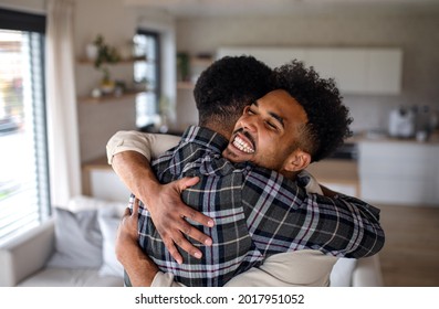 Young Happy Adult Brothers In Kitchen Indoors At Home, Hugging.