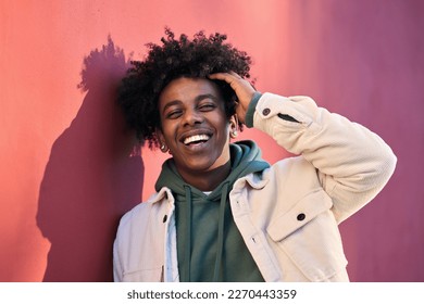 Young happy African American cool hipster guy face laughing on red city wall lit with sunlight. Smiling stylish cool rebel gen z teenager model standing outdoors. Headshot close up portrait shot. - Powered by Shutterstock