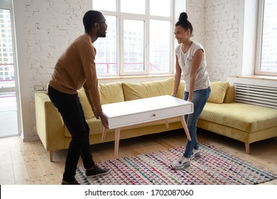 Young happy african american couple moving wooden table. Attractive family of diverse woman and man relocation furniture in new flat. Husband and wife perform permutation. First time buyers