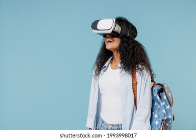 Young happy african american girl teen student wearing denim shirt backpack play game watching in vr headset pc gadget isolated on blue background Education in high school university college concept.