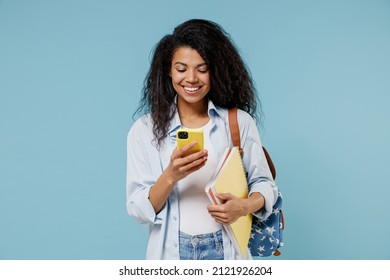 Young happy african american girl teen student in denim clothes backpack hold books using mobile cell phone chat online isolated on blue background Education in high school university college concept - Powered by Shutterstock