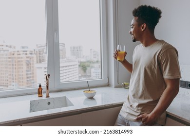 Young Happy African American Man In Casual Clothes Look Aside Drink Orange Juice Eat Breakfast Muesli Cereals With Milk Fruit In Bowl Prepare Cook Food In Kitchen At Home Indoor Healthy Diet Concept