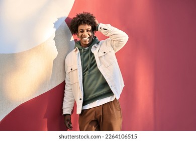 Young happy African American teen guy laughing on red wall lit with sunlight. Smiling cool ethnic generation z teenager student model standing looking at camera posing for portrait outdoors. - Powered by Shutterstock