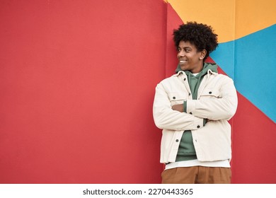 Young happy African American teen guy isolated on bright colors wall background. Smiling stylish cool ethnic generation z teenager student model standing looking away at copy space for advertising.
