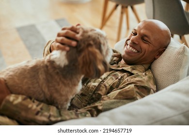 Young Happy African American Veteran Cuddling His Dog While Relaxing On The Sofa.