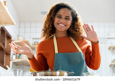 Young happy African American woman waving hands to camera while making video call in kitchen at home