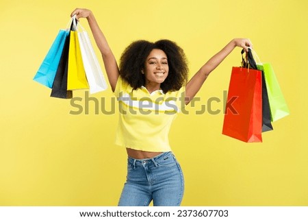 Young happy African American woman holding colorful shopping bags isolated on yellow background. Store, shopping, sales, cyber Monday concept 