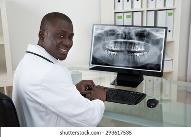 Young Happy African Dentist With Teeth X-ray On Computer At Desk