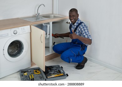 Young Happy African Male Plumber Fixing Sink In Kitchen