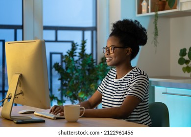 Young happy african woman freelancer in glasses working remotely in cozy home office with houseplant on background, remote female developer coding on computer, enjoying flexible freelance schedule