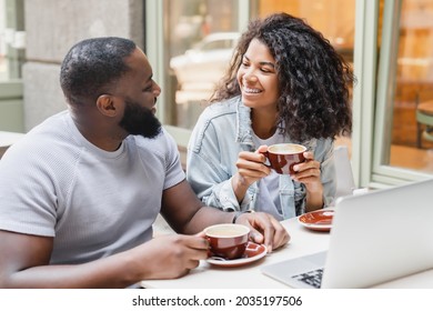 Young happy african-american couple friends talking together while drinking coffee on romantic date, watching webinars, working online on laptop in city cafe - Powered by Shutterstock