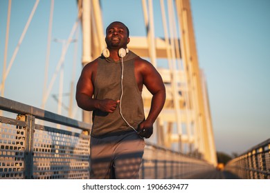 Young happy african-american man is jogging on the bridge in the city.  He is exercising to reduce his body weight. 