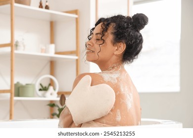 Young happy African-American woman taking bath with massage glove and soap foam at home - Powered by Shutterstock