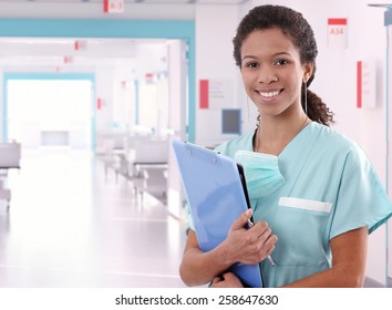 Young happy afro american nurse standing at hospital ward with clipboard and pen in hand. Smiling, looking at camera.