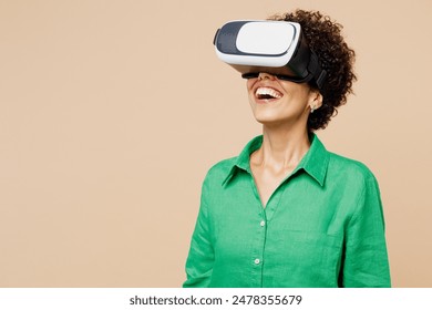 Young happy amazed fun woman of African American ethnicity wear green shirt casual clothes watching in vr headset pc gadget isolated on plain pastel light beige background studio. Lifestyle concept - Powered by Shutterstock