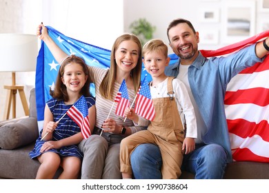 Young happy american family parents and two little kids sitting on sofa at home with flags of united states and smiling at camera while celebrating Independence Day. Patriotic US holiday concept - Powered by Shutterstock