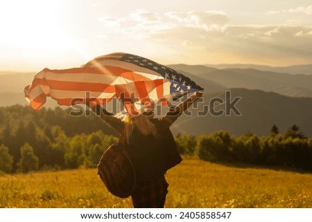 Young happy american woman with long hair holding waving on wind USA national flag on her sholders relaxing outdoors enjoying warm summer day