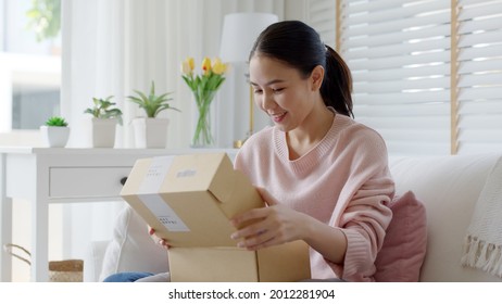 Young happy asia people teen girl smile enjoy unbox post mail sit relax at home comfort sofa couch feel joy amazed awe wow in omni channel fast send parcel via online sale shop store e-commerce order. - Powered by Shutterstock