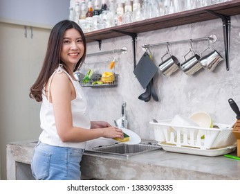 young  happy Asia woman is washing dishes while doing cleaning at home