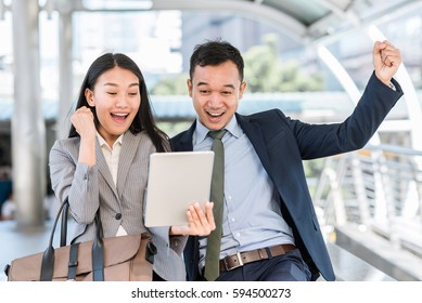 Young Happy Asian Businessman And Woman Celebrated Success While Looking In Tablet Outdoor.