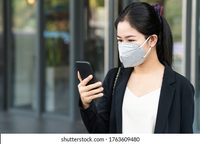 Young happy asian businesswoman worker wearing safety medical n95 facemask smiling and look at mobile phone in concept resume and back to work after covid crisis, find job after get lay off concept. - Powered by Shutterstock